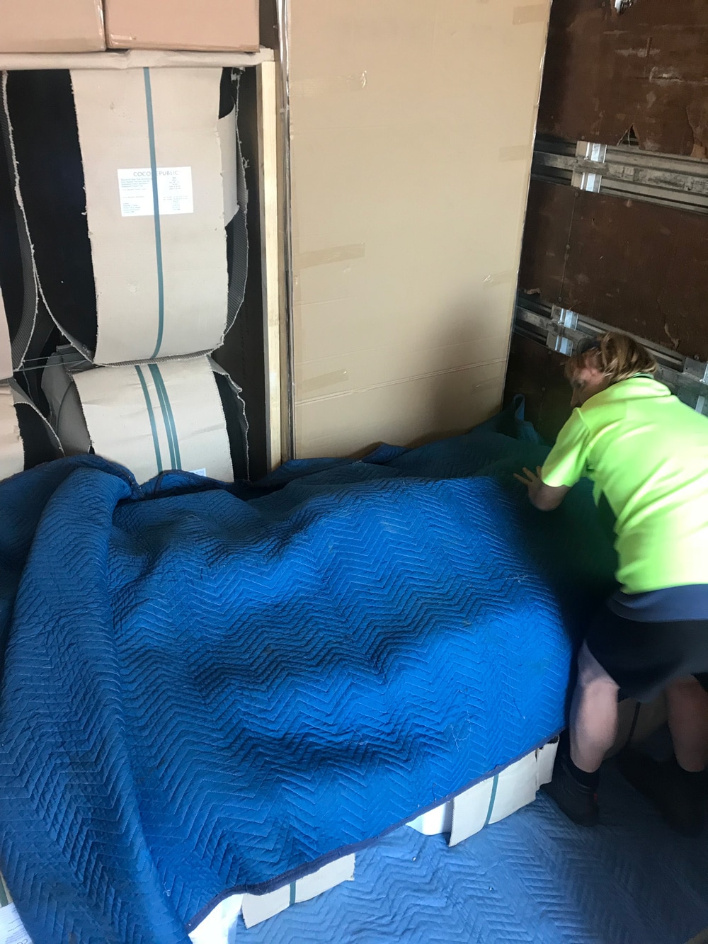 Furniture items wrapped in blue moving blankets with worker securing load – Melbourne to Sydney run