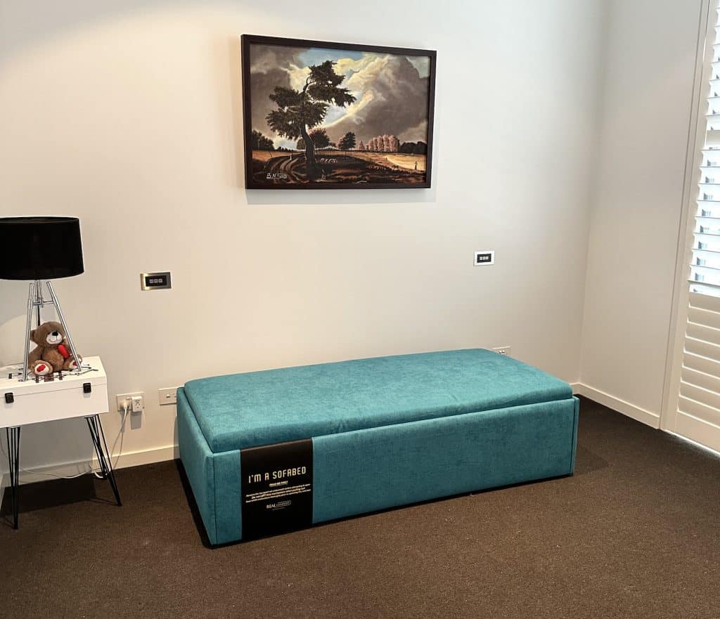 Teal Zara Queen Ottoman Bed beside window shutters and a side table in Albert Park.