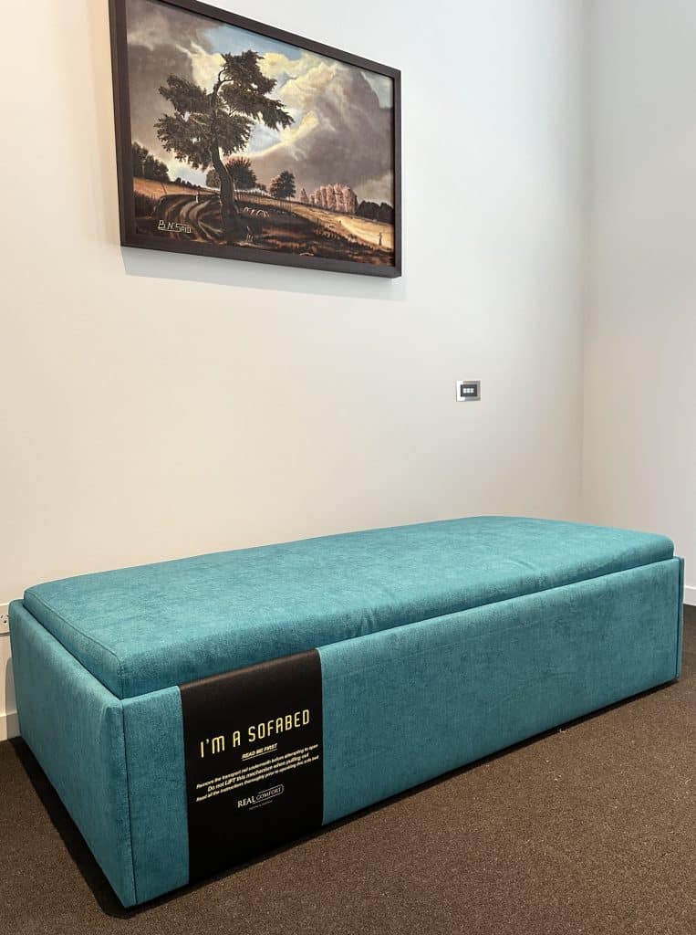 Three-quarter view of the teal Zara Queen Ottoman Bed in Albert Park, showing its product instruction label.