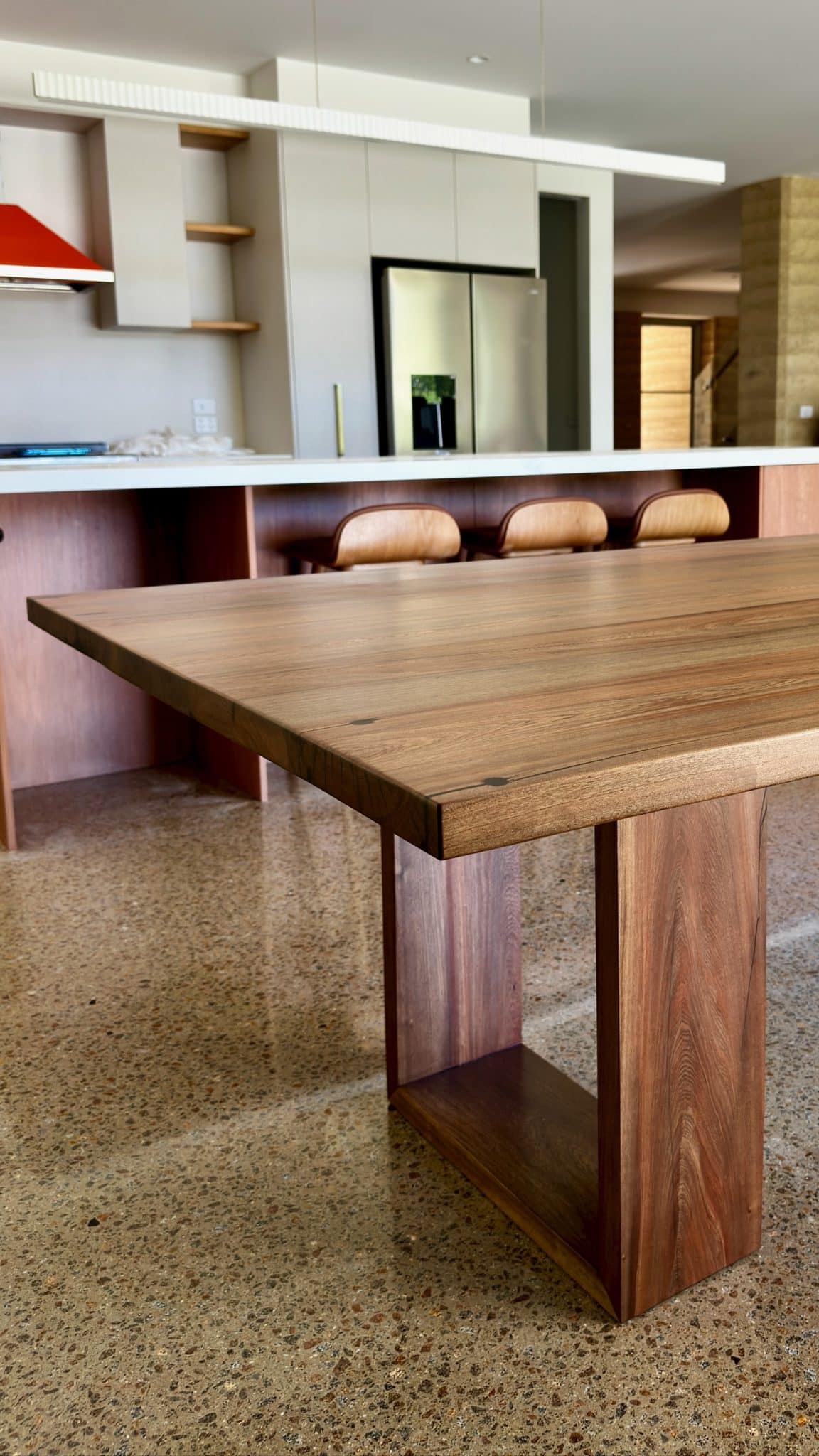 timber dining table end detail with seating in the background.