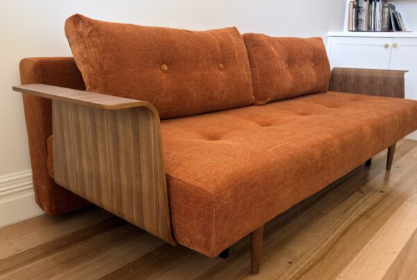 Rust-coloured Innovation Living Recast sofa bed with curved timber arms and buttoned cushions, delivered to Coburg by Phil’s Furniture Freighters.