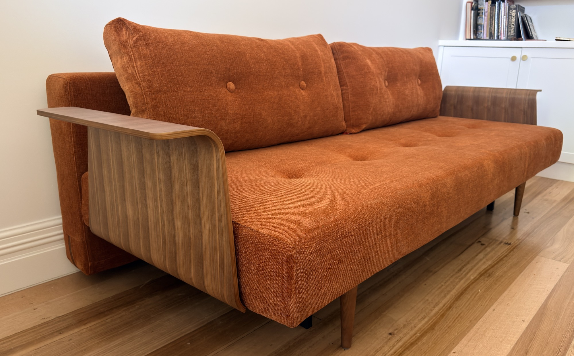 Rust-coloured Innovation Living Recast sofa bed with curved timber arms and buttoned cushions, delivered to Coburg by Phil’s Furniture Freighters.