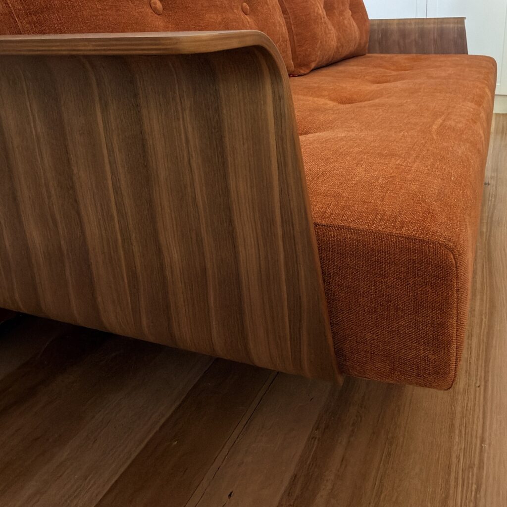 Close side view of the curved timber arm and rust-coloured upholstery on a Recast sofa bed in Coburg.