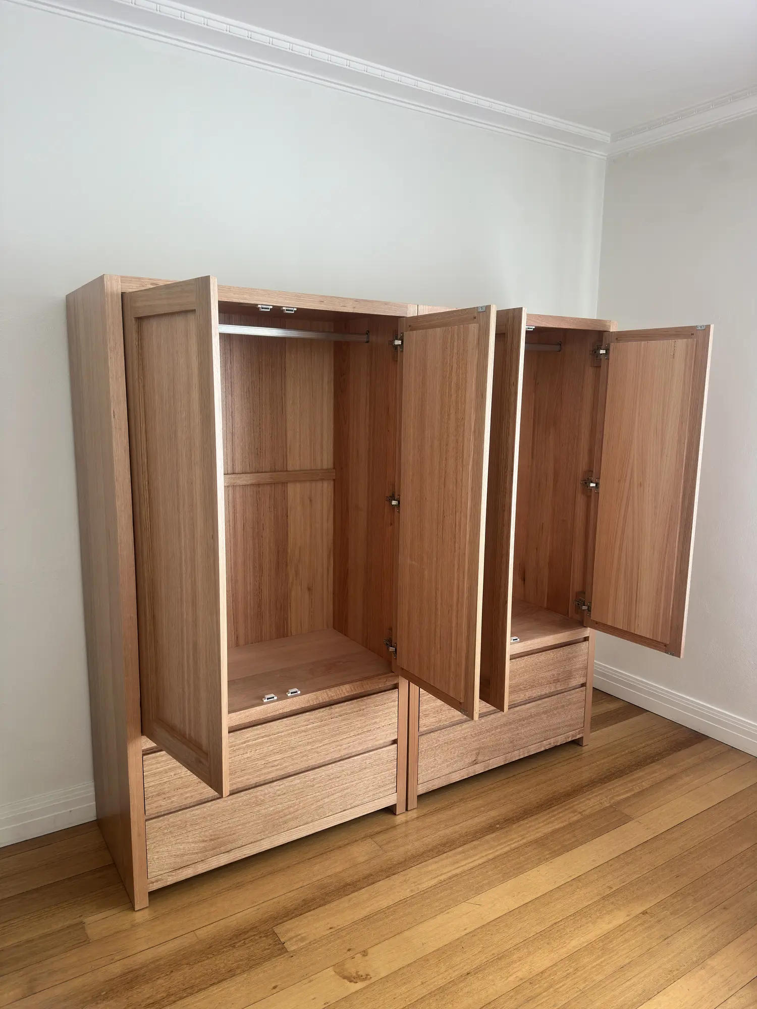 Timber wardrobes with open doors showing hanging rails above the lower drawers.
