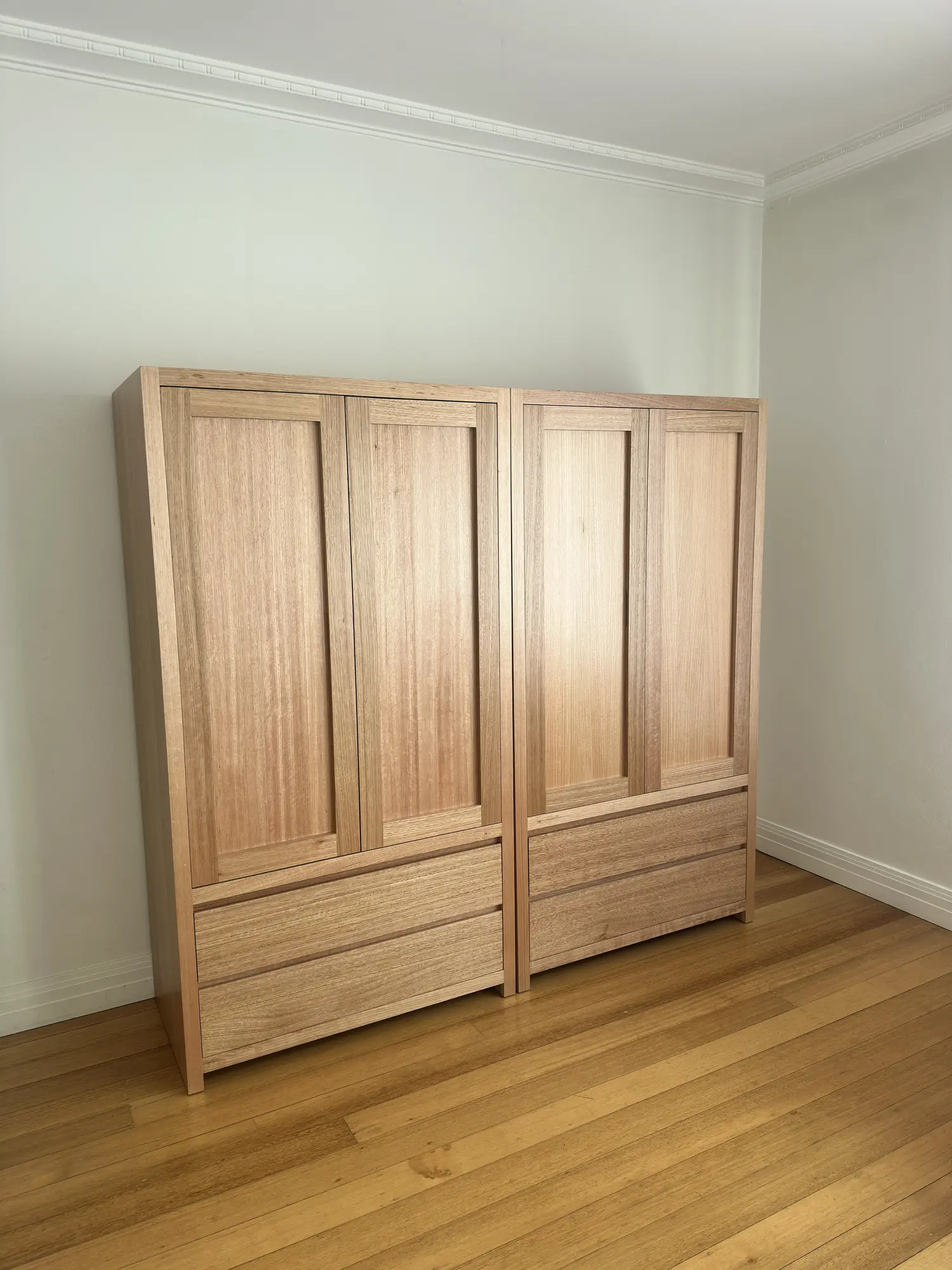Two timber wardrobes with closed panelled doors and lower drawers in a South Yarra room.
